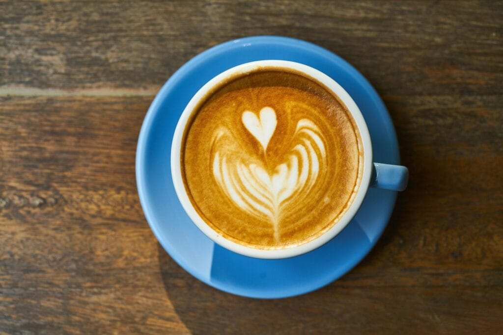 Top view of a latte with heart art in a blue cup on a wooden table.