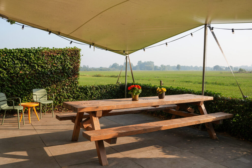 Terras met picknicktafel en stoelen met prachtig uitzicht op een groen weiland bij vergaderlocatie Ruimte voor Inzicht in Oisterwijk