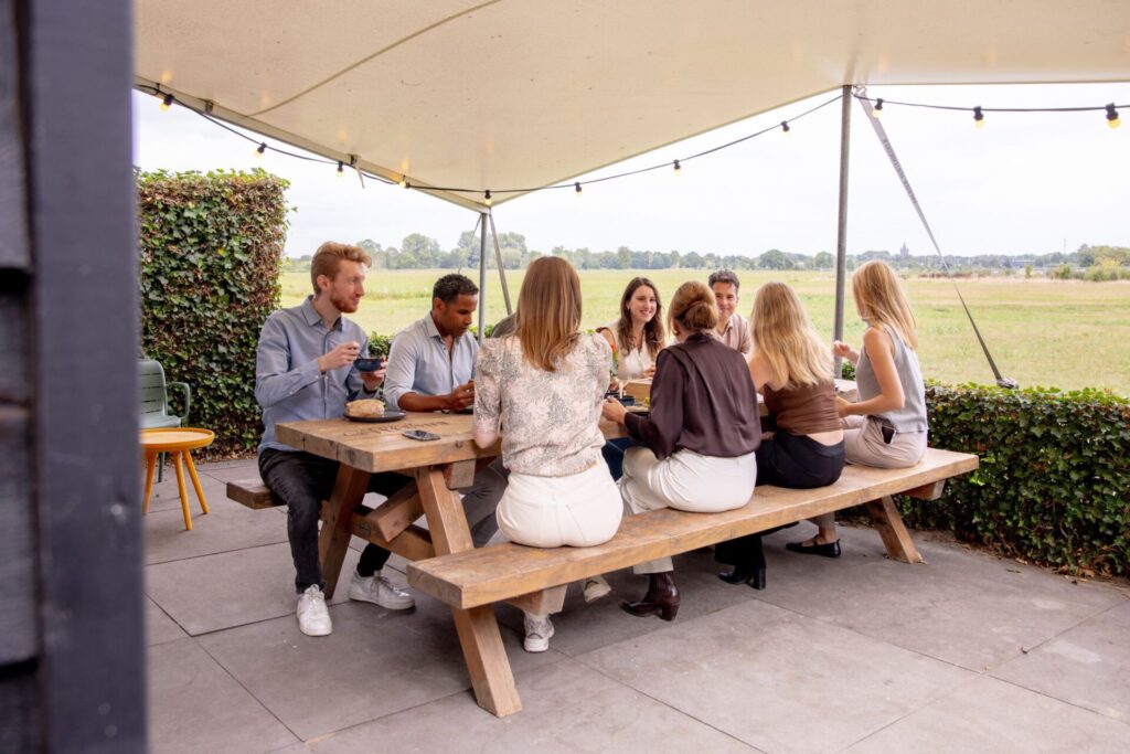 Groep mensen die samen op het terras zitten te praten en te lunchen bij vergaderlocatie Ruimte voor Inzicht in Oisterwijk