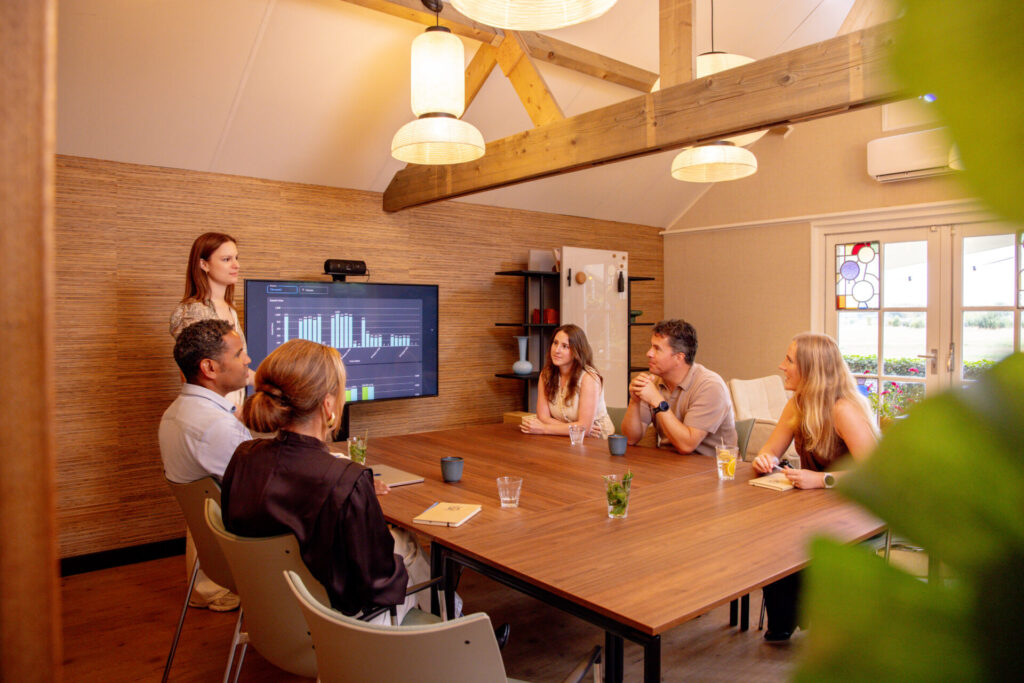 Groep mensen die een vergadering houden bij Ruimte voor Inzicht in Oisterwijk. Er staat een vrouw die presenteert voor een leuke groep mensen.