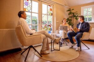Drie mensen die een gesprek met elkaar voeren op comfortabele stoelen in vergaderlocatie Ruimte voor Inzicht in Oisterwijk