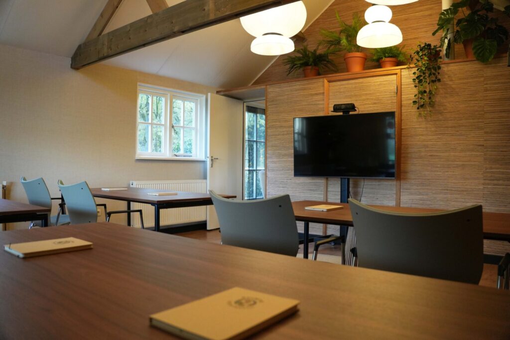 School opstelling met comfortabele stoelen, een kleed en een verrijdbaar beeldscherm in een warme ruimte bij vergaderlocatie Ruimte voor Inzicht in Oisterwijk