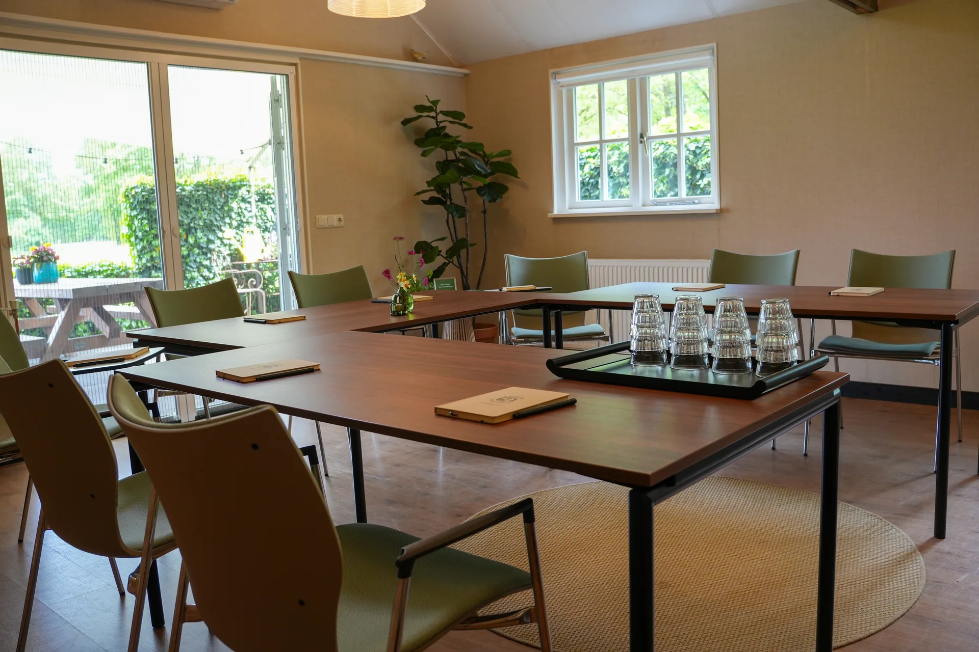 U-opstelling met comfortabele stoelen, een kleed en een glasbord in een warme ruimte bij vergaderlocatie Ruimte voor Inzicht in Oisterwijk